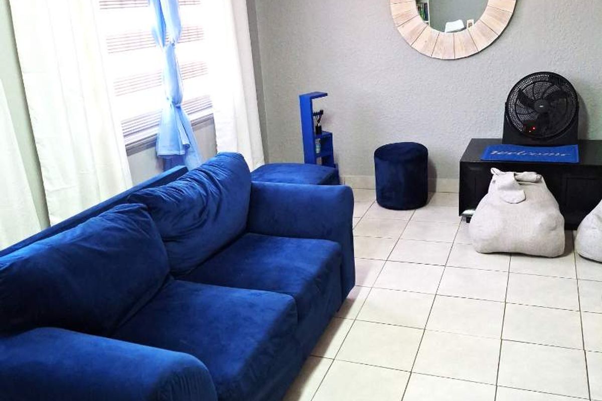 A living room featuring tiled flooring, neutral wall finishes, and large windows with fitted blinds.