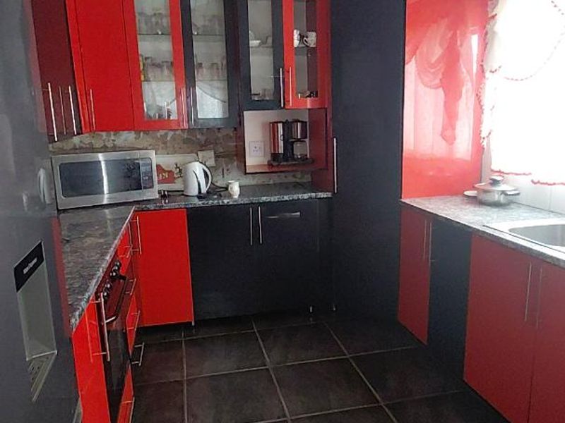 A functional kitchen featuring high-contrast red and black cabinetry, dark floor tiles, and a panelled ceiling, with a dedicated space for built-in appliances.