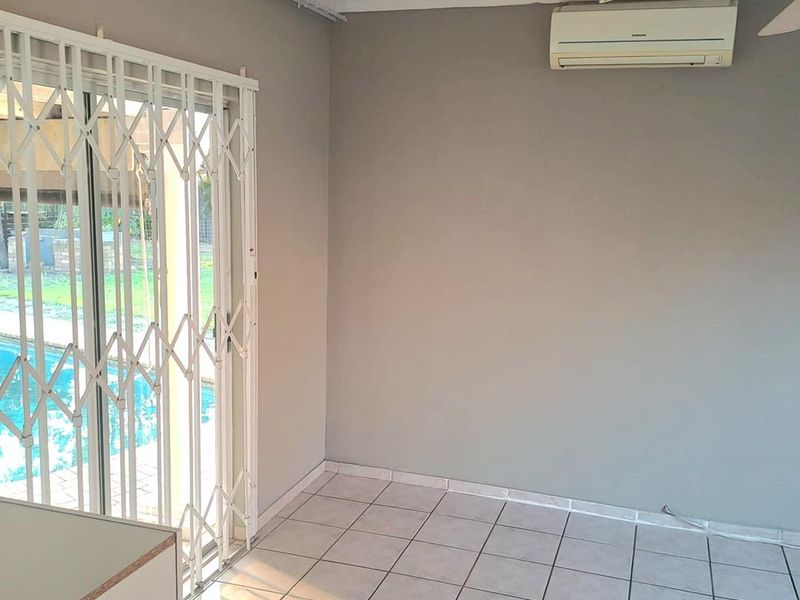 An empty living area featuring tiled floors, a wall-mounted air conditioning unit, and a sliding glass door with a security gate leading outdoors.