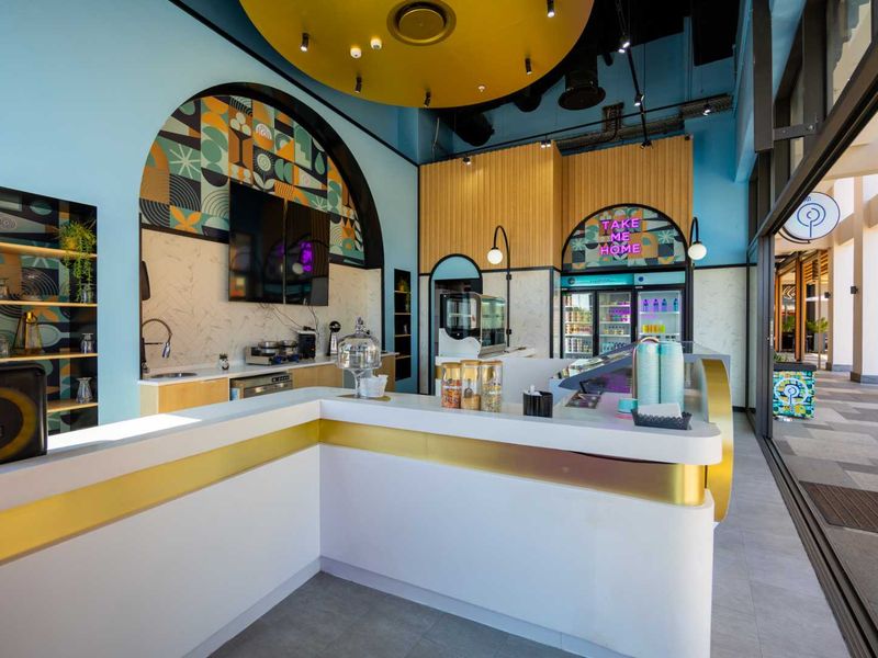 Modern commercial service counter area featuring integrated refrigeration, stylish decorative wall paneling, and recessed ceiling lighting in a well-maintained retail space.