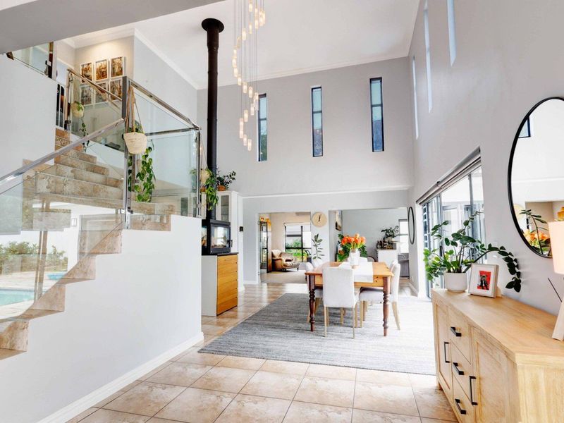 Spacious open-plan living and dining area featuring a striking staircase with glass balustrades, high ceilings, and a modern freestanding fireplace.