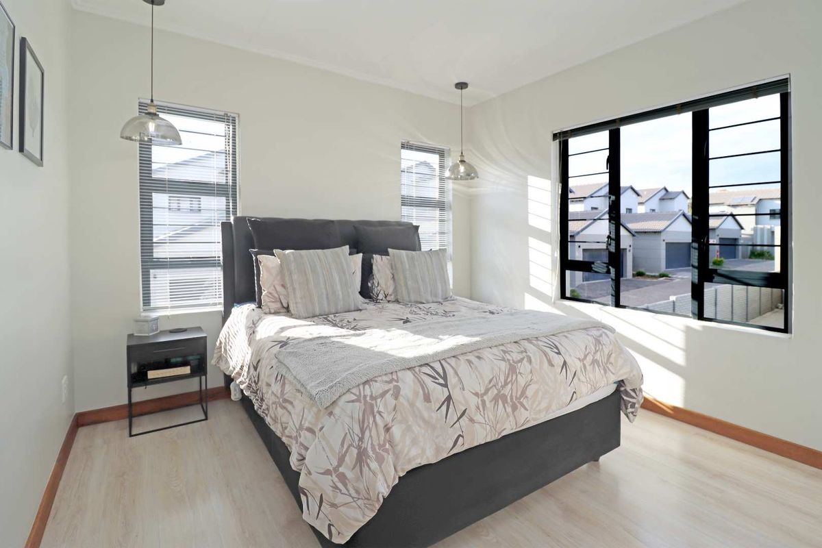 A bright and modern bedroom featuring light wood-look flooring, large windows with black frames, and contemporary pendant lighting.