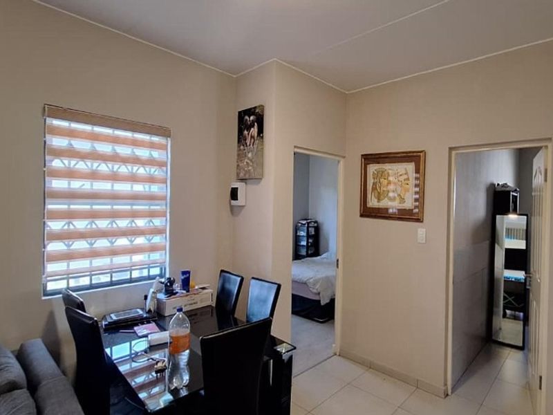 A functional living area featuring tiled flooring, neutral wall tones, and a window fitted with modern zebra blinds and security bars.