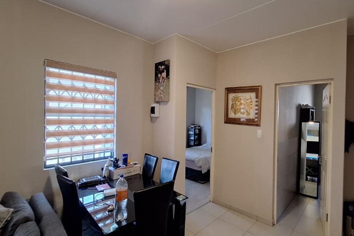 A functional living area featuring tiled flooring, neutral wall tones, and a window fitted with modern zebra blinds and security bars.