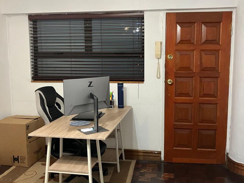 A functional home office space featuring classic parquet flooring, a solid timber door, and venetian blinds, offering a practical layout for remote work.