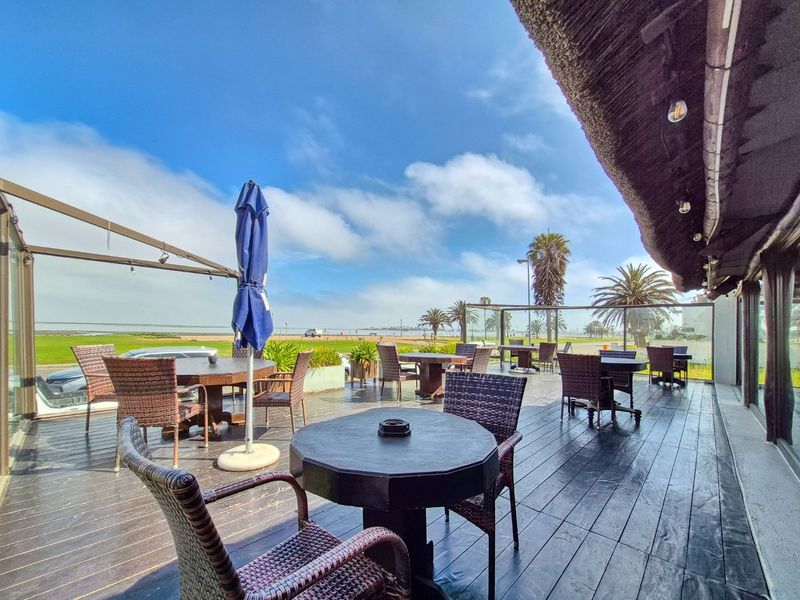 Spacious outdoor patio featuring timber decking, a thatched roof covering, and a glass balustrade with scenic coastal views.