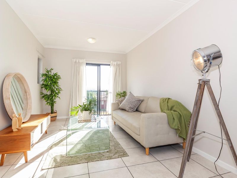 A bright and well-maintained living room featuring neutral tiled flooring and a sliding glass door providing access to an outdoor balcony.