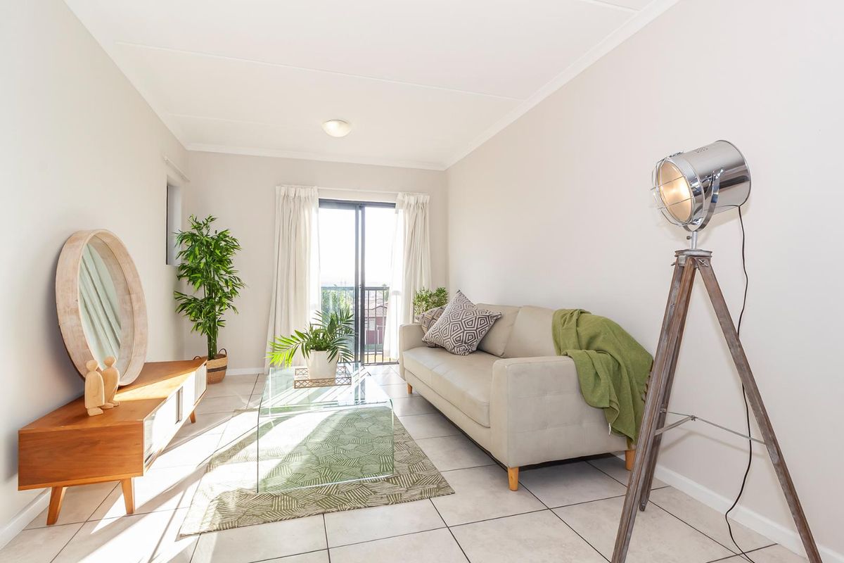 A bright and well-maintained living room featuring neutral tiled flooring and a sliding glass door providing access to an outdoor balcony.