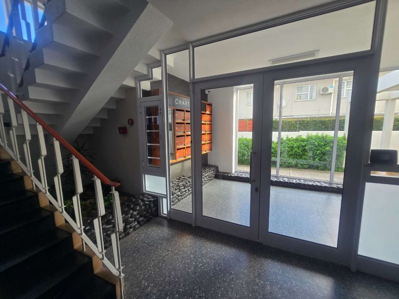 A clean and well-maintained apartment building entrance lobby featuring terrazzo flooring, glass double doors, and a staircase with a metal handrail.