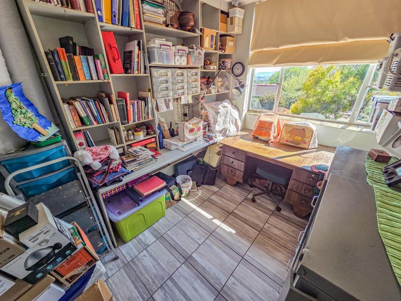 A functional home office space featuring built-in shelving units, tiled flooring, and a large window providing natural light and an exterior view.