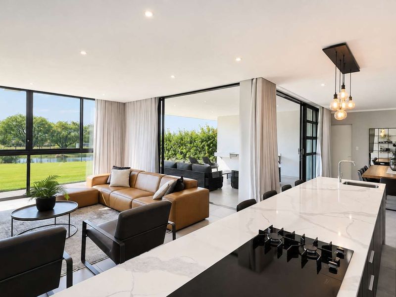Modern open-plan living area featuring a sleek kitchen island with stone countertops, gas cooktop, and seamless flow to a covered patio with garden views.