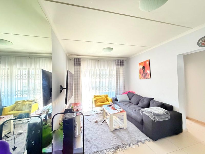 A living room featuring tiled flooring, a large mirrored wall panel, and a sliding glass door with a security gate leading to the exterior.