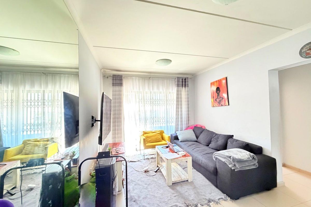 A living room featuring tiled flooring, a large mirrored wall panel, and a sliding glass door with a security gate leading to the exterior.