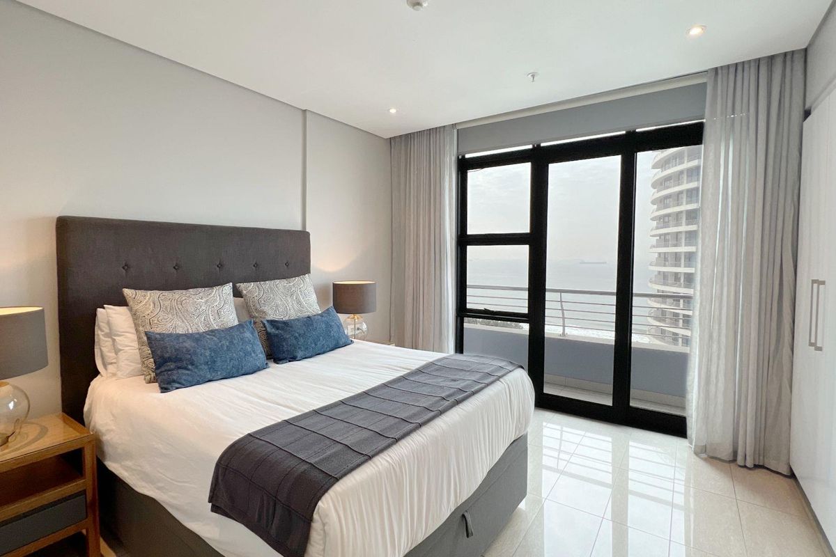 Modern bedroom featuring large floor-to-ceiling windows with balcony access, sleek tiled flooring, and built-in wardrobe storage.