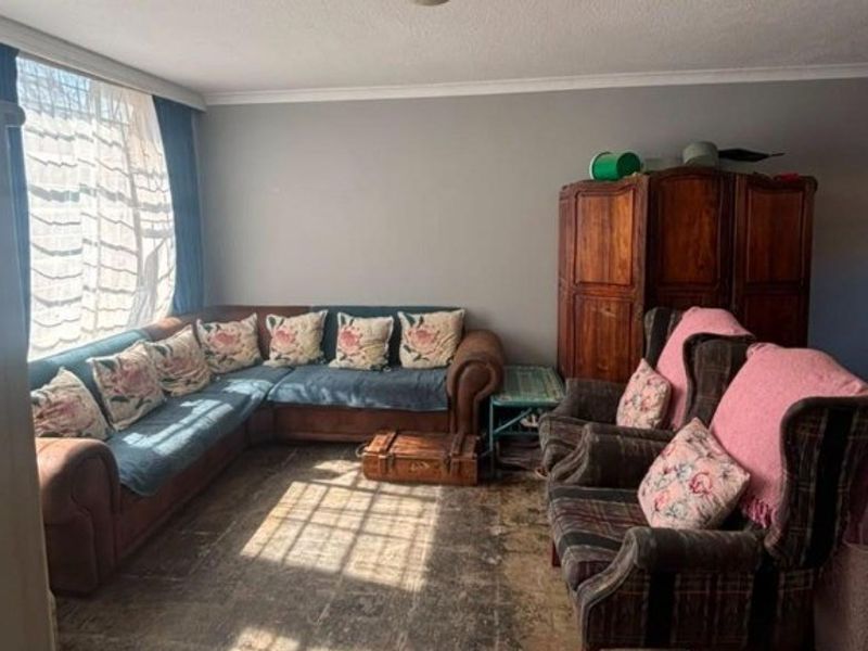 A living room featuring a large window and coving, currently showing signs of wear on the flooring.