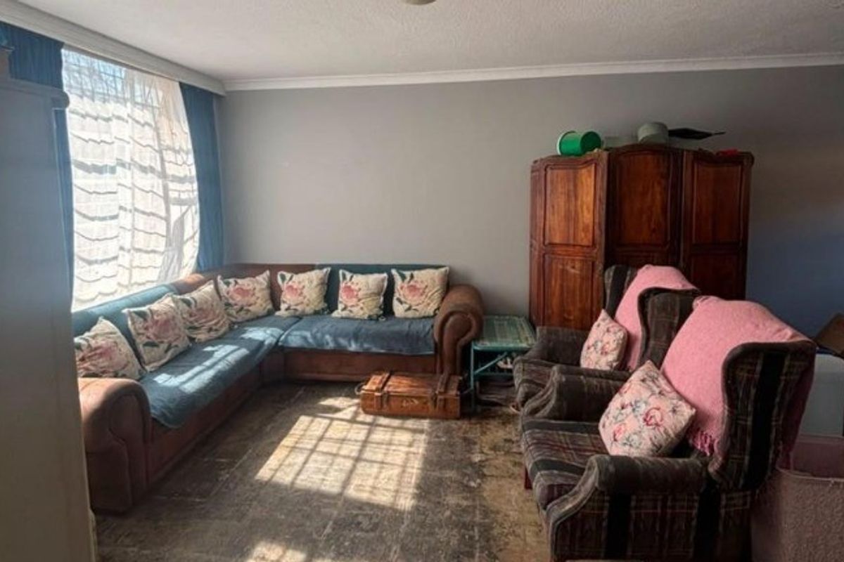 A living room featuring a large window and coving, currently showing signs of wear on the flooring.