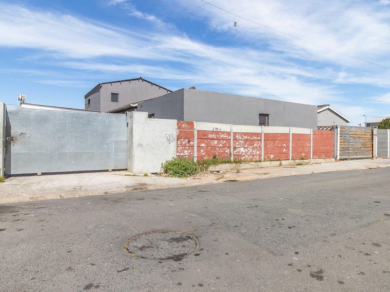 Street view of the property frontage featuring a metal sliding gate and a precast concrete boundary wall with visible signs of weathering.
