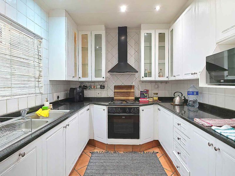 A functional kitchen featuring white cabinetry, dark granite countertops, a built-in oven with extractor fan, and tiled finishes throughout.