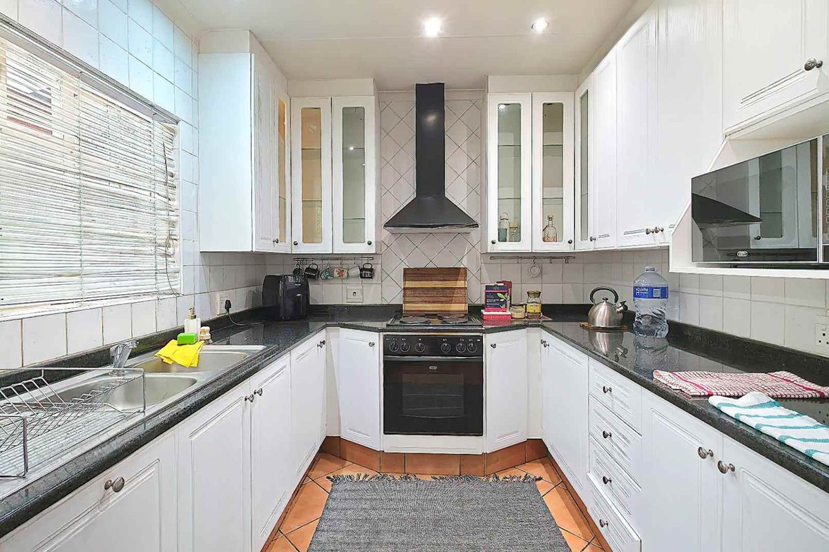 A functional kitchen featuring white cabinetry, dark granite countertops, a built-in oven with extractor fan, and tiled finishes throughout.