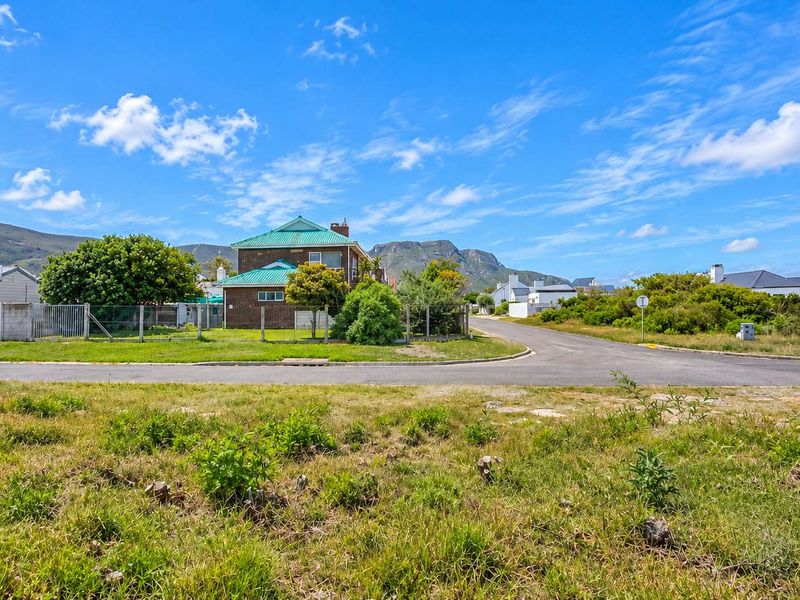 A view of a vacant residential plot featuring natural grass cover, situated on a corner lot with established neighborhood infrastructure and mountain views.