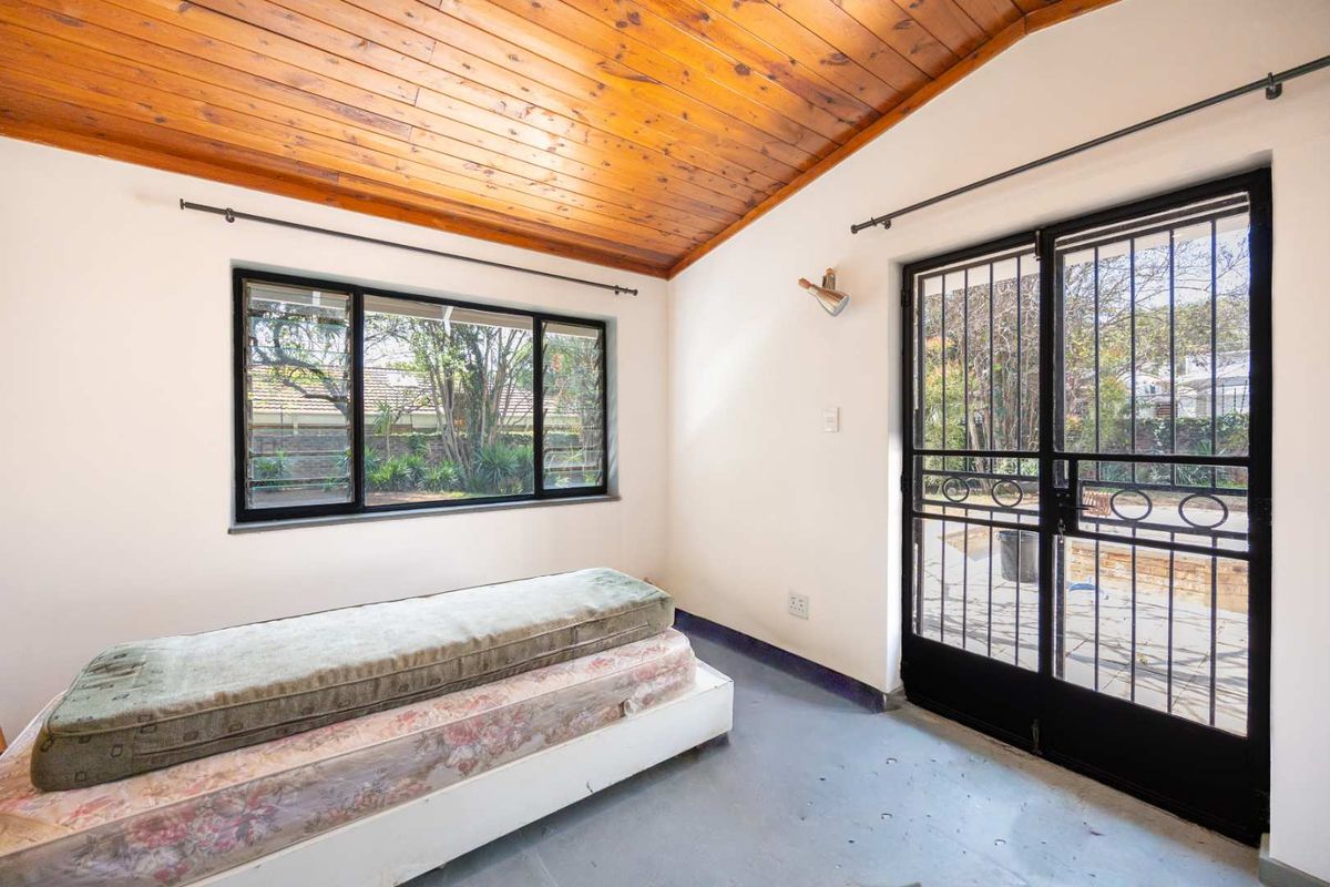 A bedroom featuring a timber-clad ceiling, security gate access to the exterior, and large windows providing natural light.