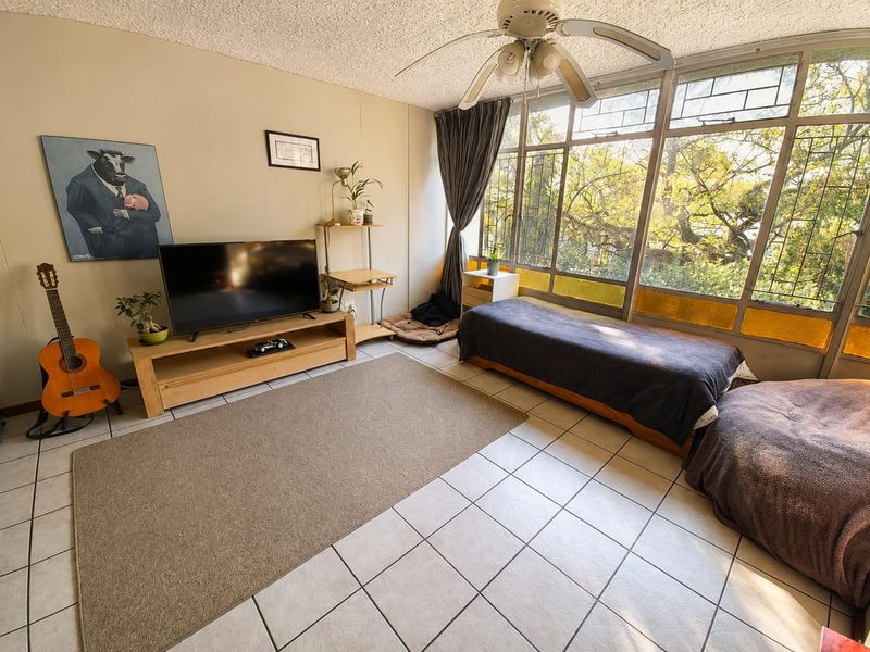 Living room featuring large multi-pane windows, ceramic tile flooring, and a ceiling fan, offering a bright space with potential for modernization.