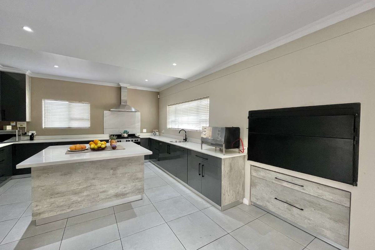Modern kitchen featuring a central island, sleek cabinetry, stone countertops, built-in oven, extractor fan, and tiled flooring.