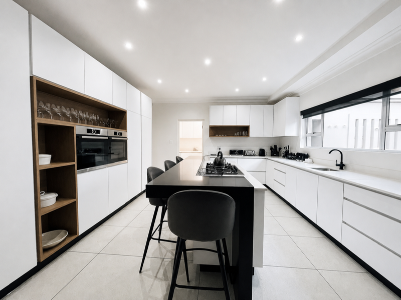 Modern kitchen featuring sleek white cabinetry, a central island with a breakfast bar, integrated ovens, and high-quality stone countertops.