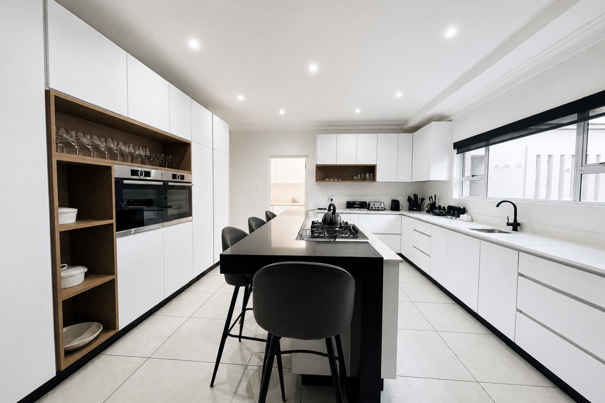 Modern kitchen featuring sleek white cabinetry, a central island with a breakfast bar, integrated ovens, and high-quality stone countertops.