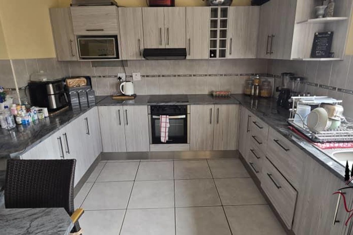 A functional U-shaped kitchen featuring light wood-grain cabinetry, granite countertops, tiled flooring, and integrated oven and hob.