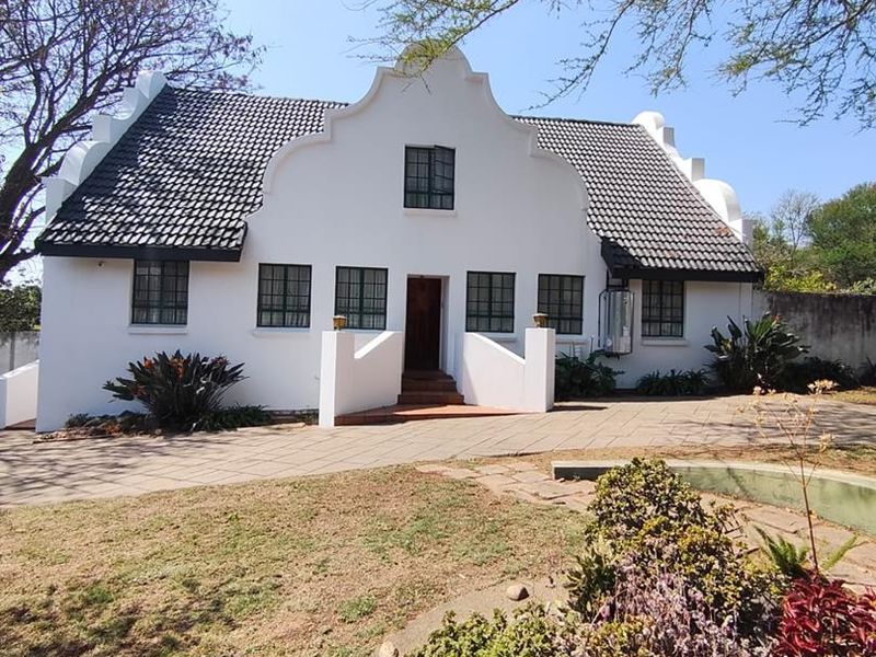 A well-maintained Cape Dutch style home featuring a distinctive gabled facade, tiled roof, and a paved driveway set within a landscaped garden.