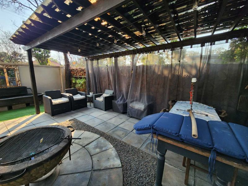 A covered outdoor patio area featuring a timber pergola, stone wall, and a built-in fire pit, ideal for outdoor entertaining.