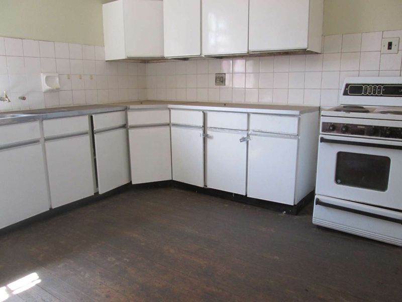 A dated, empty kitchen featuring white cabinetry, a tiled backsplash, and a freestanding stove, requiring renovation to modernize the space.