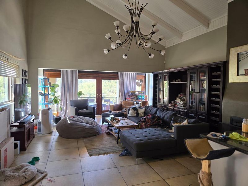Spacious living room featuring a high vaulted ceiling with exposed beams, tiled flooring, built-in cabinetry, and large sliding glass doors leading to the outdoors.