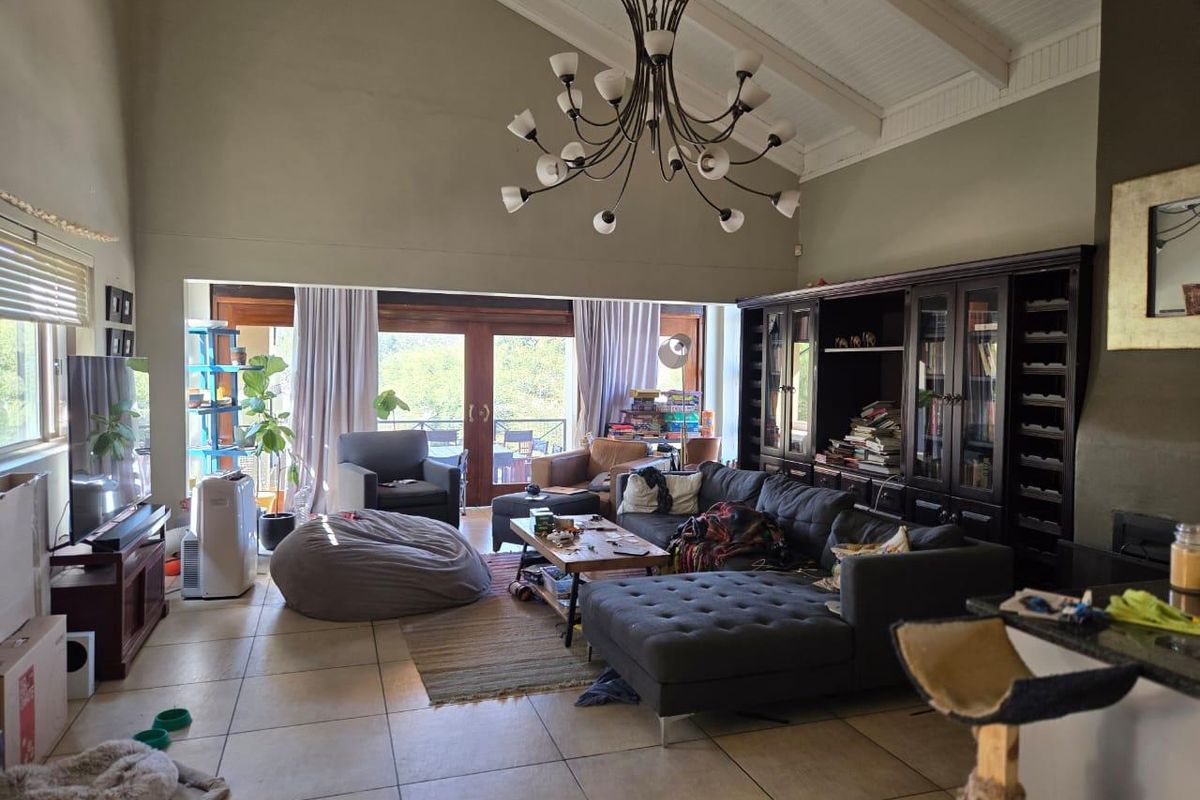 Spacious living room featuring a high vaulted ceiling with exposed beams, tiled flooring, built-in cabinetry, and large sliding glass doors leading to the outdoors.