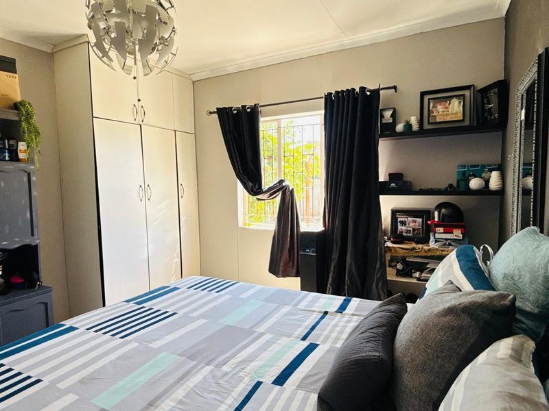 A functional bedroom featuring built-in cupboards, a window with security bars, and a central ceiling light fixture.