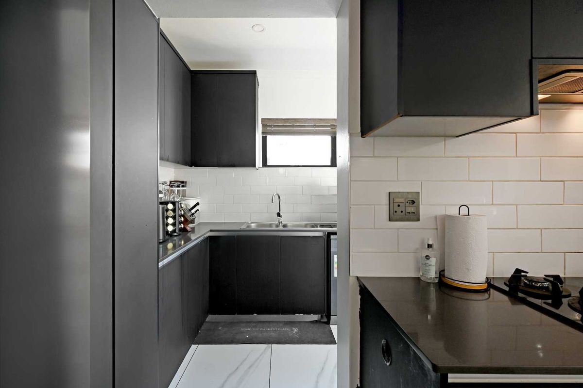 Modern kitchen featuring sleek black cabinetry, white subway tile backsplash, stone countertops, and integrated gas hob with extractor fan.