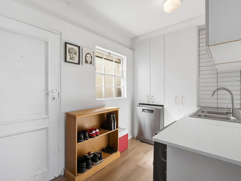 A functional scullery featuring white built-in cabinetry, a stainless steel sink, integrated dishwasher, and subway tile backsplash with modern laminate flooring.