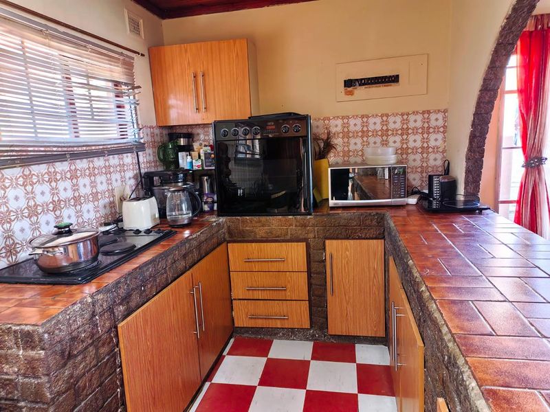 A compact kitchen featuring dated tiled countertops, wood-finish cabinetry, and a built-in oven with a hob, offering potential for a modern renovation.