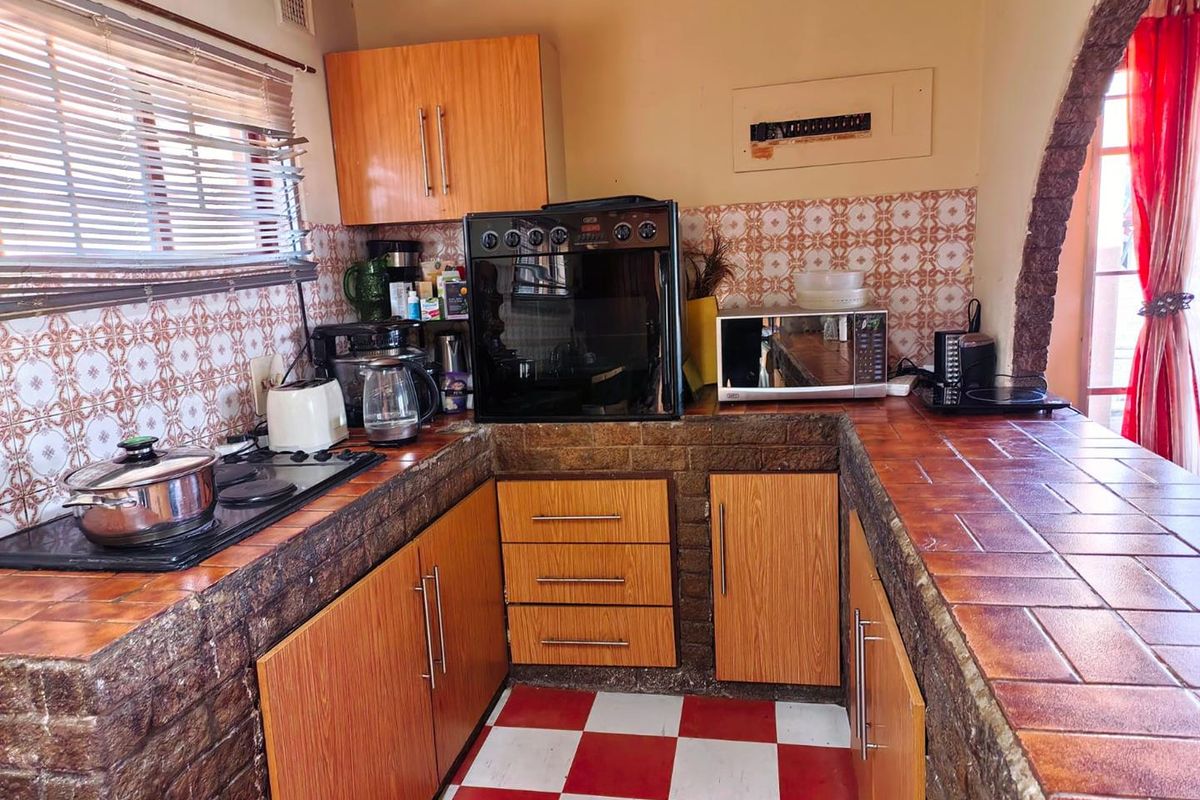 A compact kitchen featuring dated tiled countertops, wood-finish cabinetry, and a built-in oven with a hob, offering potential for a modern renovation.