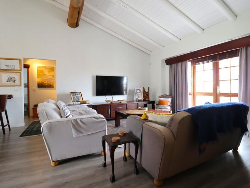 Spacious living room featuring a vaulted ceiling with exposed timber beam, laminate flooring, and large timber-framed glass doors leading to the exterior.
