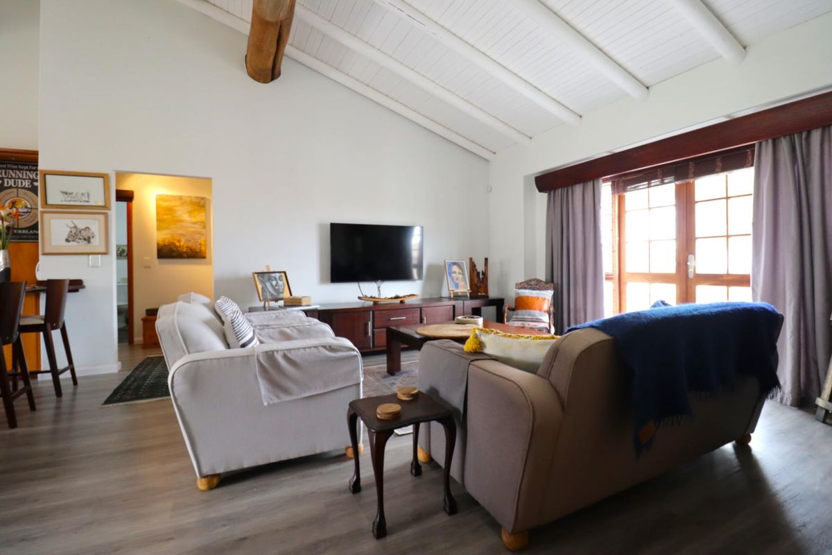 Spacious living room featuring a vaulted ceiling with exposed timber beam, laminate flooring, and large timber-framed glass doors leading to the exterior.