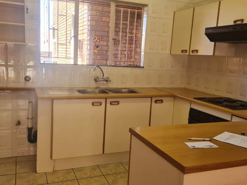 A functional kitchen featuring double bowl sink, built-in cabinetry, laminate countertops, and integrated hob with extractor fan, finished with tiled splashbacks and flooring.