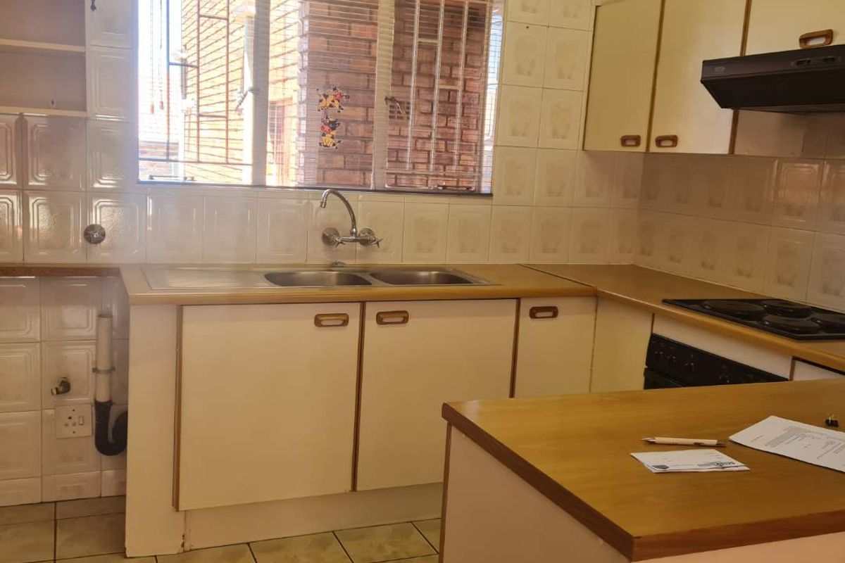 A functional kitchen featuring double bowl sink, built-in cabinetry, laminate countertops, and integrated hob with extractor fan, finished with tiled splashbacks and flooring.