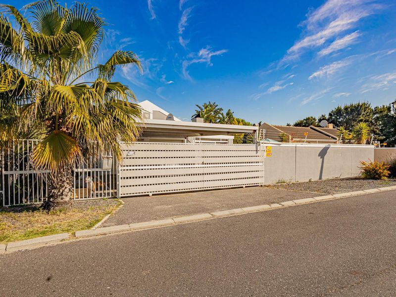 Front exterior view of the property featuring a secure sliding gate, perimeter wall with electric fencing, and a paved driveway with carport.