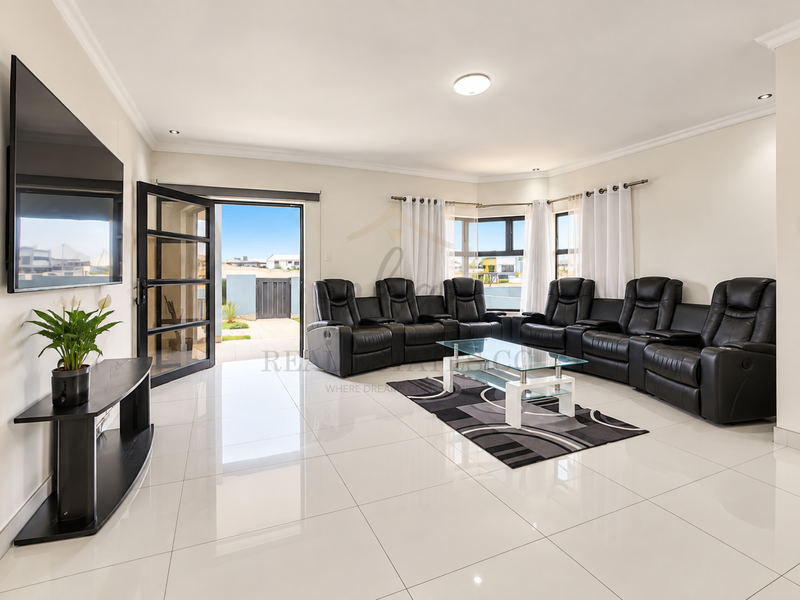 Spacious living room featuring polished porcelain floor tiles, modern recessed lighting, and large aluminium-framed glass doors providing seamless access to the outdoor area.