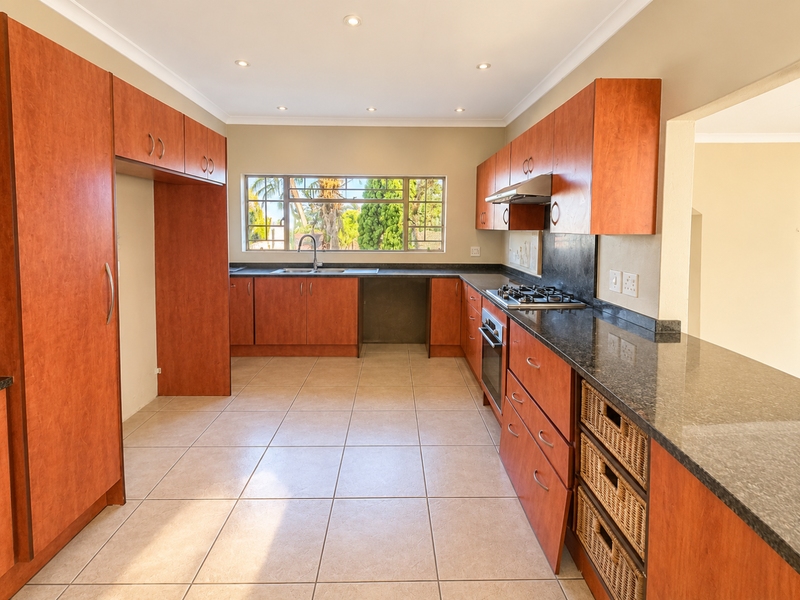A spacious kitchen featuring cherry-wood cabinetry, granite countertops, a gas hob, and an integrated oven, with ample natural light and tiled flooring.