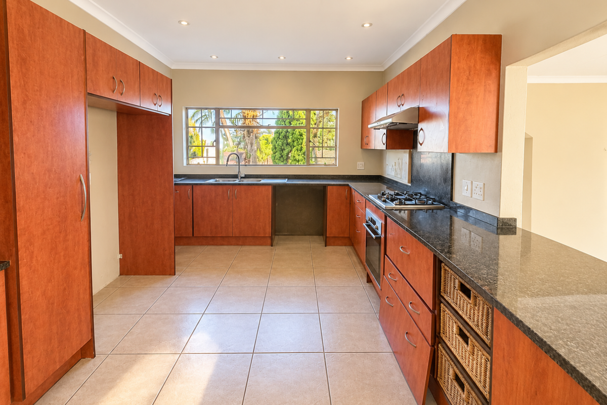 A spacious kitchen featuring cherry-wood cabinetry, granite countertops, a gas hob, and an integrated oven, with ample natural light and tiled flooring.