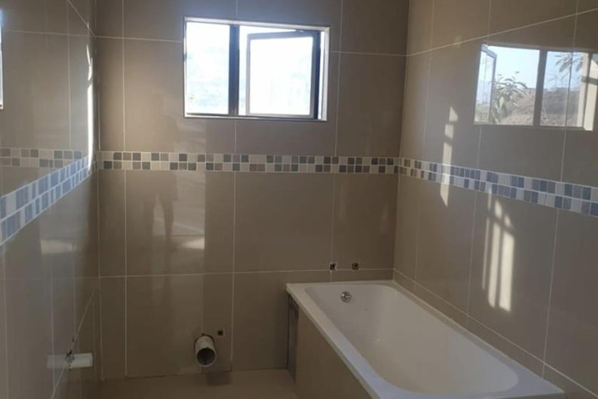 A partially completed bathroom featuring full-height ceramic wall tiles, a built-in bathtub, and a casement window, currently awaiting final plumbing and finishing touches.