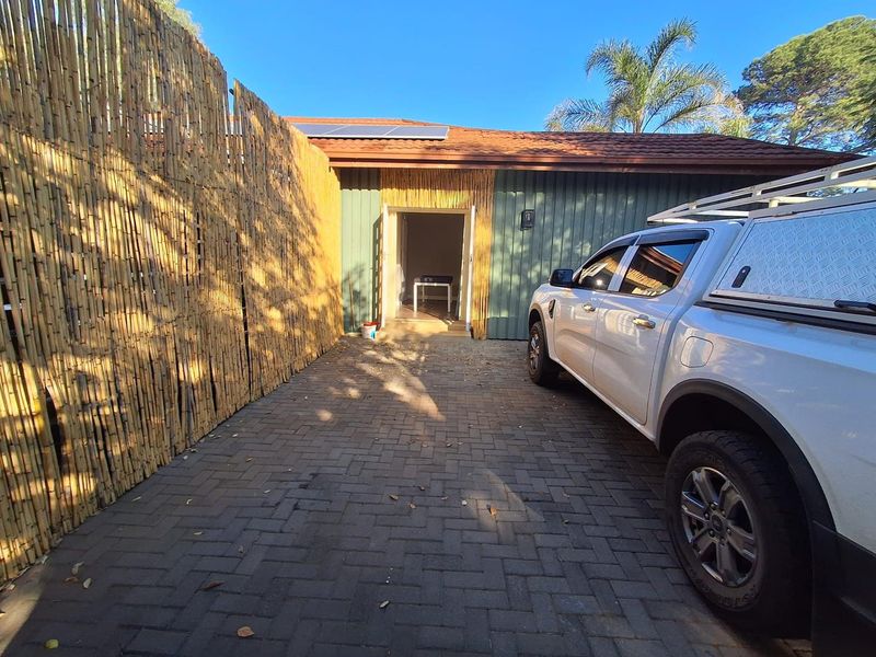 Front exterior view featuring a paved driveway, bamboo privacy screening, and timber-clad facade with solar panels installed on the tiled roof.